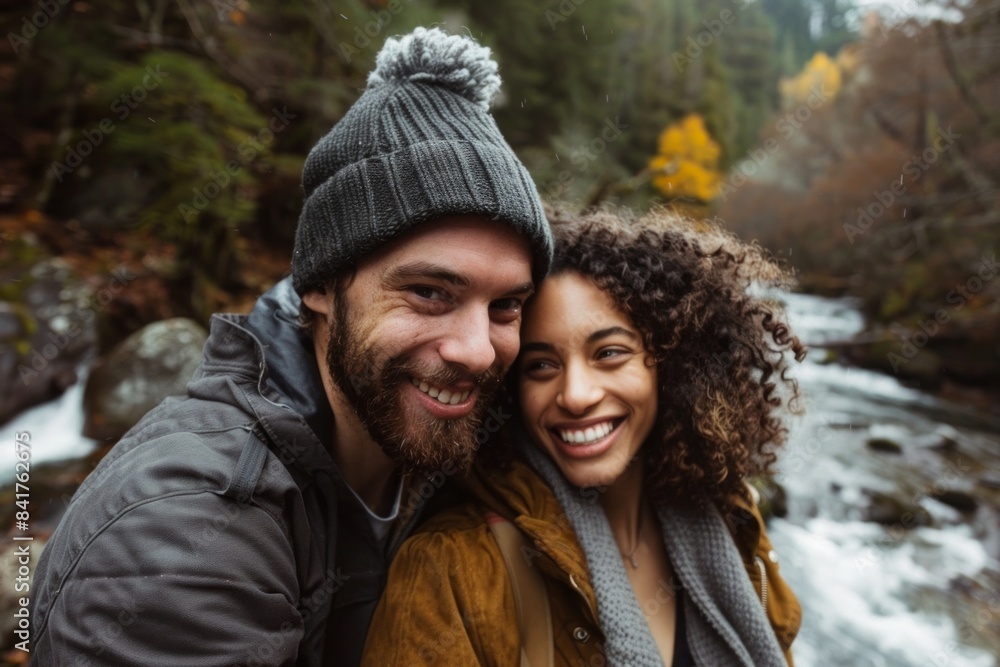 Portrait of a happy multiethnic couple in their 20s donning a warm wool beanie in front of tranquil forest stream Portrait of a happy multiethnic couple in their 20s donning a warm wool beanie in front of tranquil forest stream