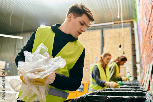 Obraz na plátně Young volunteer in yellow vest sorts trash into bin with eco-conscious team, making a positive environmental impact