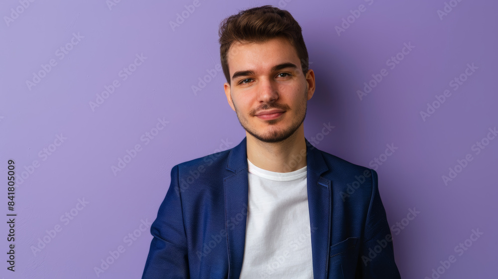 A young man in a white shirt and blue blazer smiles confidently while standing against a pastel purple background. A young man in a white shirt and blue blazer smiles confidently while standing against a pastel purple background.