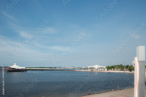 A view of the deserted ancol beach, which is serene with a wooden jetty jutting out into the calm waters. A white canopy structure stands at the end of the pier.