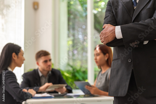 Canvas Print A man in a suit stands with his arms crossed in front of a group of people