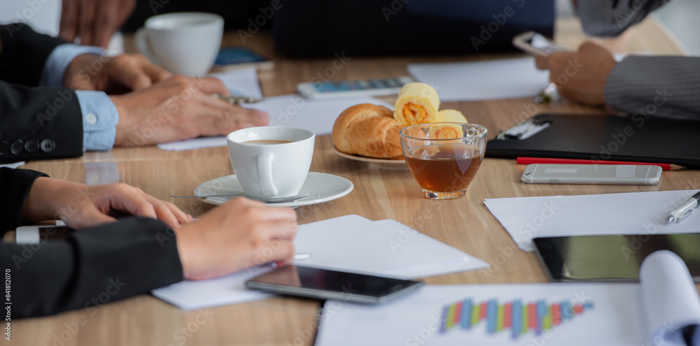 A group of people are sitting around a table having a meeting. There are croissants, coffee, and tea on the table. A group of people are sitting around a table having a meeting. There are croissants, coffee, and tea on the table.