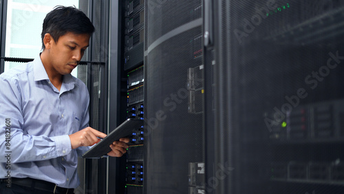 A technician in a blue shirt uses a tablet while inspecting a server rack in a modern data center, ensuring proper functionality.