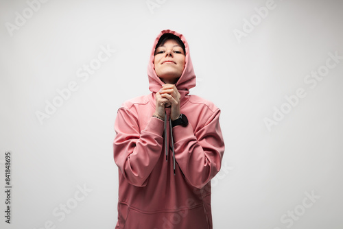 Young woman in pink hoodie standing against a plain background with a thoughtful expression