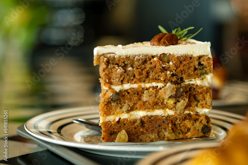 Close-up of one delicious slice of carrot cake with cream cheese frosting, topped with pecan and sprig of rosemary, served on plate photo