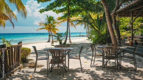 A table and chairs are set up on a sandy beach with palm trees in the background and a view of the ocean