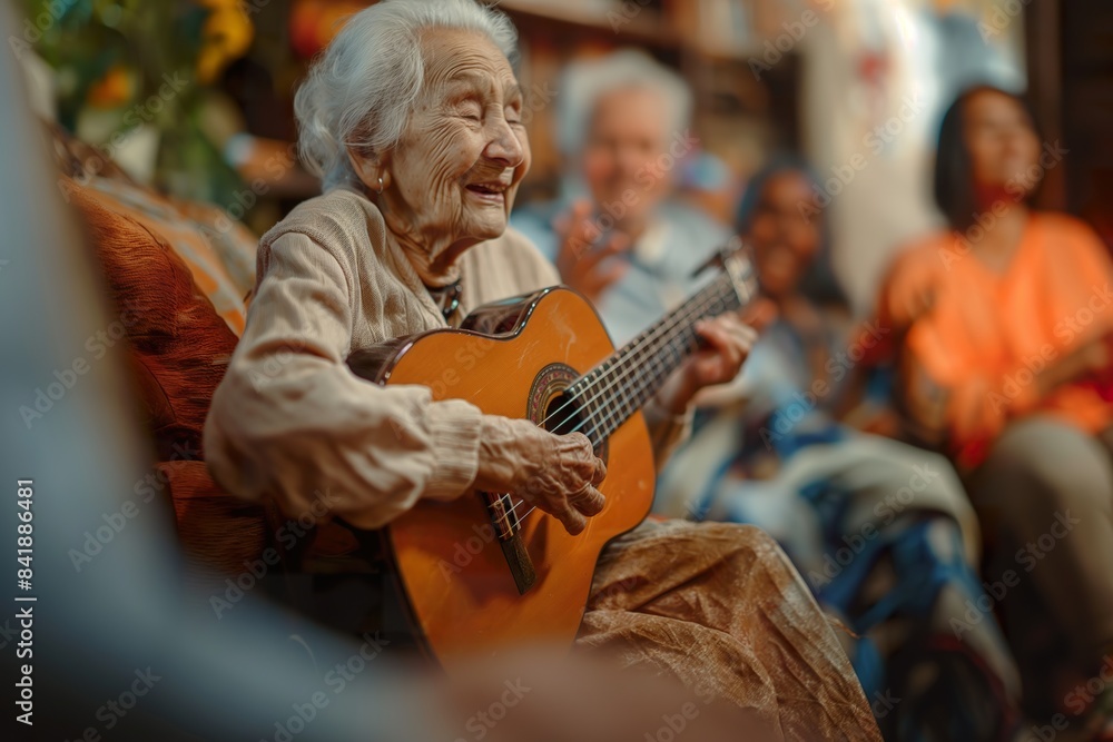 An elderly woman, seated on a couch, plays a guitar with a warm smile, surrounded by other people in a cozy living room. An elderly woman, seated on a couch, plays a guitar with a warm smile, surrounded by other people in a cozy living room.