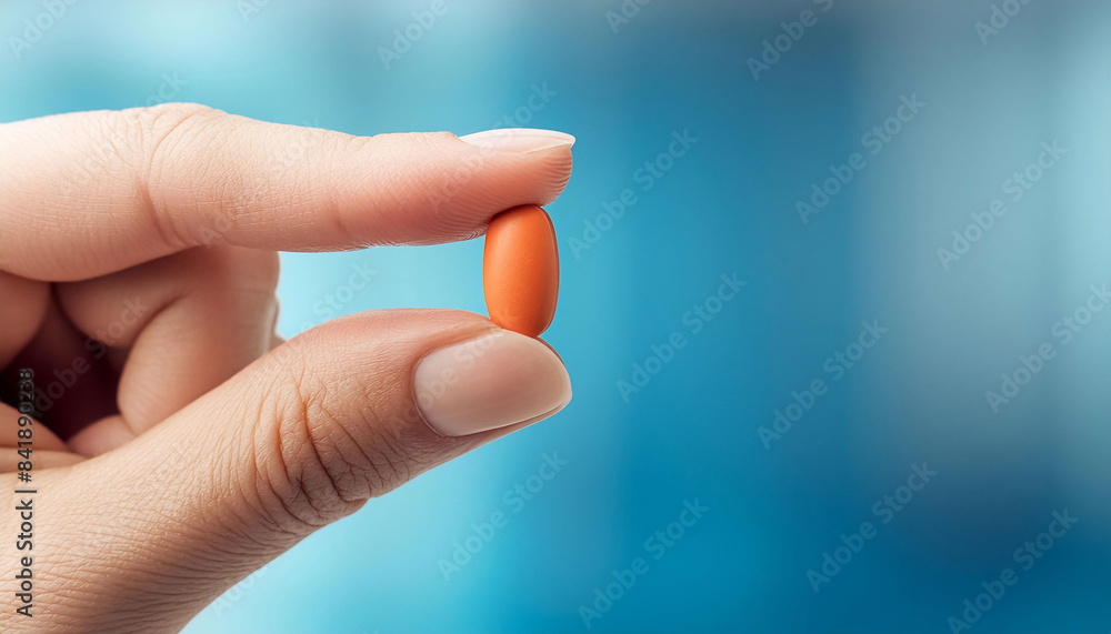Close-up of a hand holding an orange oval-shaped tablet between the thumb and index finger Medicine Pharmaceuticals healthcare treatment Close-up of a hand holding an orange oval-shaped tablet between the thumb and index finger Medicine Pharmaceuticals healthcare treatment