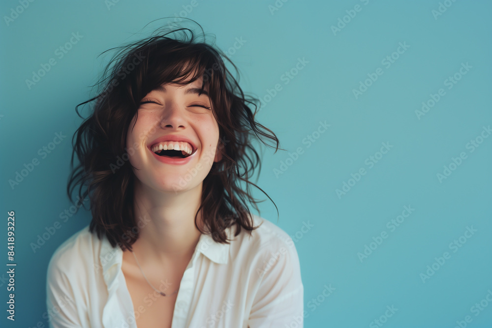 A laughing woman with her head tilted back against a pastel blue background A laughing woman with her head tilted back against a pastel blue background