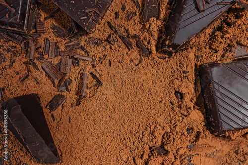 Slices and shaves of dark bitter chocolate scattered on cocoa powder background, top view photo
