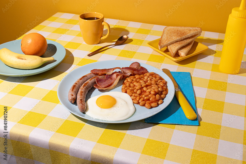 Yellow coloured Tablecloth with a delicious full English Breakfast, egg, beans, sausages and bacon, some toasted bread slices, fruit and a cup of coffee Yellow coloured Tablecloth with a delicious full English Breakfast, egg, beans, sausages and bacon, some toasted bread slices, fruit and a cup of coffee