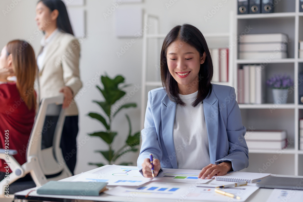 Businesswoman in a modern office environment working at her desk with colleagues in the background, showcasing teamwork and productivity. Businesswoman in a modern office environment working at her desk with colleagues in the background, showcasing teamwork and productivity.