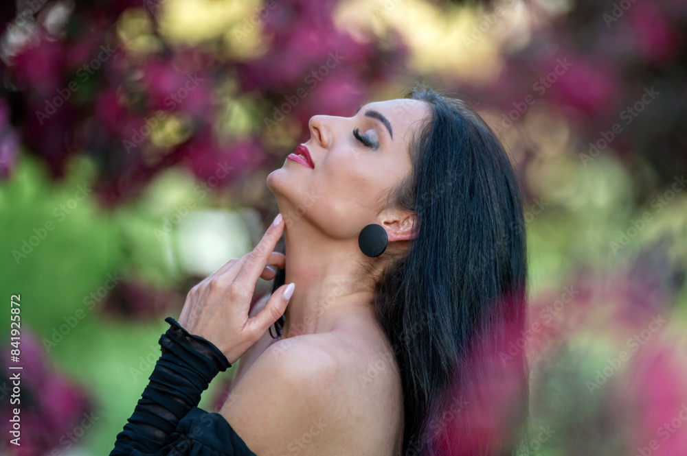 Fototapeta premium Woman posing in a garden with flowers. Blurred background with copy space