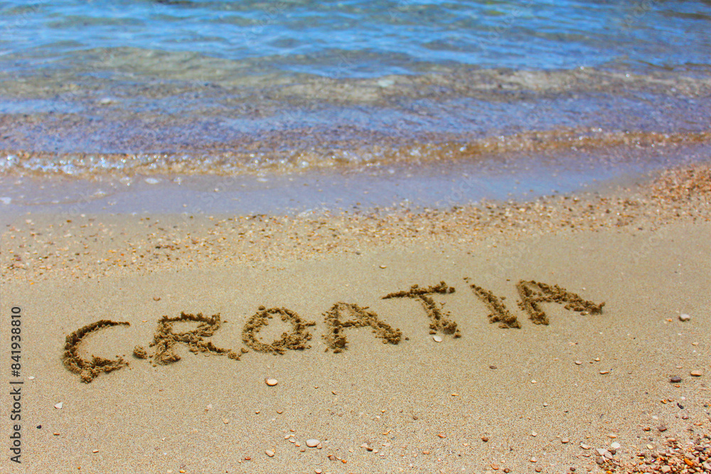 Fototapeta premium Croatia delicately inscribed in sandy beach as waves approach. Blue sea glistens under summer sun, creating idyllic scene. Tranquil waters and sandy shores inspire beach vacation