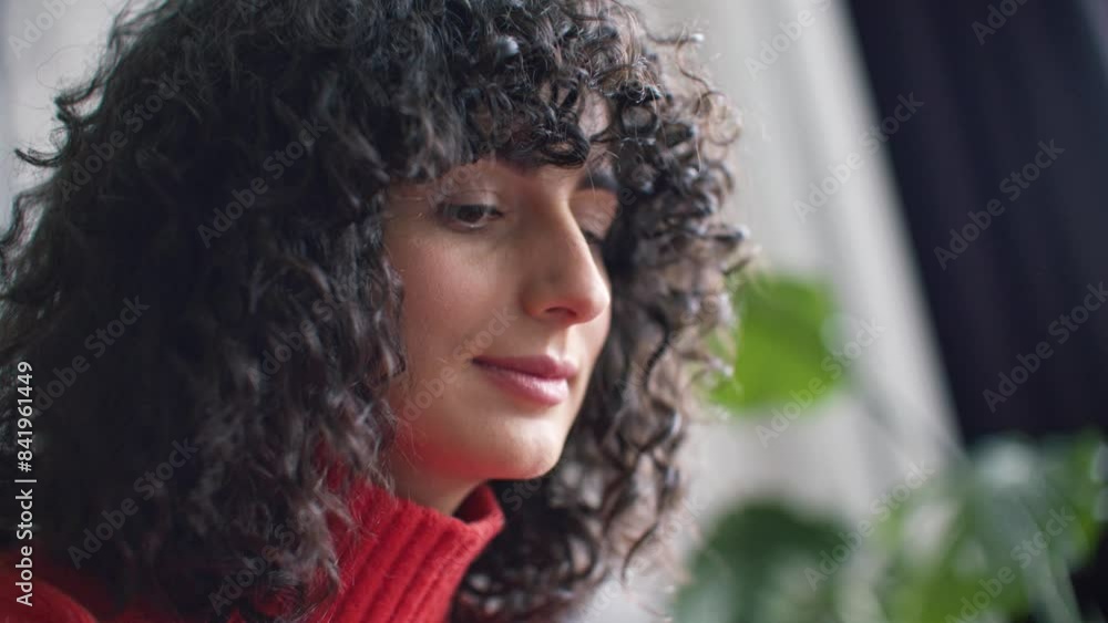 Side facial view of Caucasian female with curly black hair. Woman smirking while looking at something in front of her. Holding one hand under her chin. Focused person working in office. Side facial view of Caucasian female with curly black hair. Woman smirking while looking at something in front of her. Holding one hand under her chin. Focused person working in office.