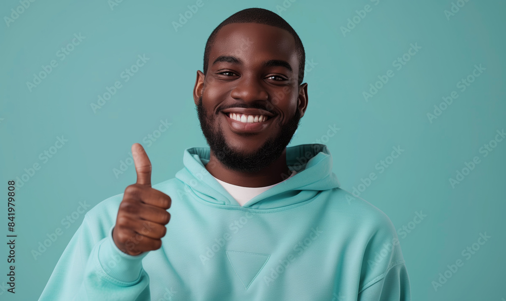 Young african american man in a sweatshirt smiling with healthy teeth showing thumb up at copy space expressing wow emotion standing isolated on mint background Young african american man in a sweatshirt smiling with healthy teeth showing thumb up at copy space expressing wow emotion standing isolated on mint background