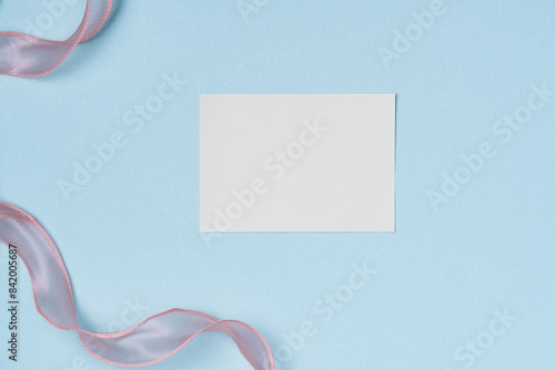 White paper list with pink ribbon on blue background from above. Copy space