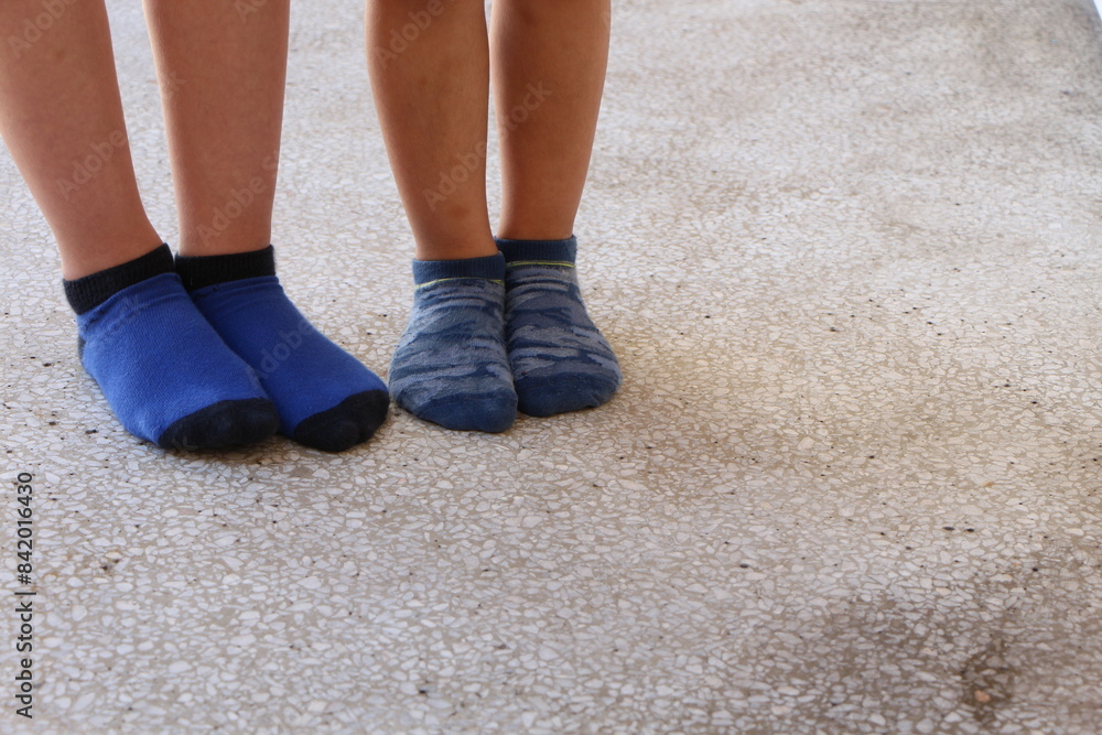 Feet of two kids standing on concrete floor. One child wear navy and indigo blue socks and the other child wear blue camouflage print socks. Feet of two kids standing on concrete floor. One child wear navy and indigo blue socks and the other child wear blue camouflage print socks.