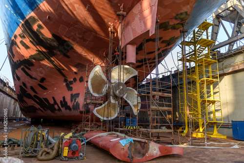 Cargo vessel in dry dock on ship repairing yard. Variable pitch propeller and rudder. Welder working on ship repairing yard.