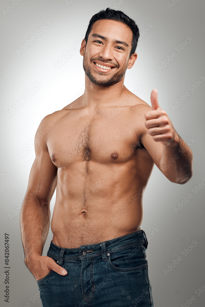 Fototapeta premium Thumbs up, fitness and Asian man in portrait with smile, body positivity and topless in studio. Happy person, approval and proud of progress from exercise, wellness and goal on gray background