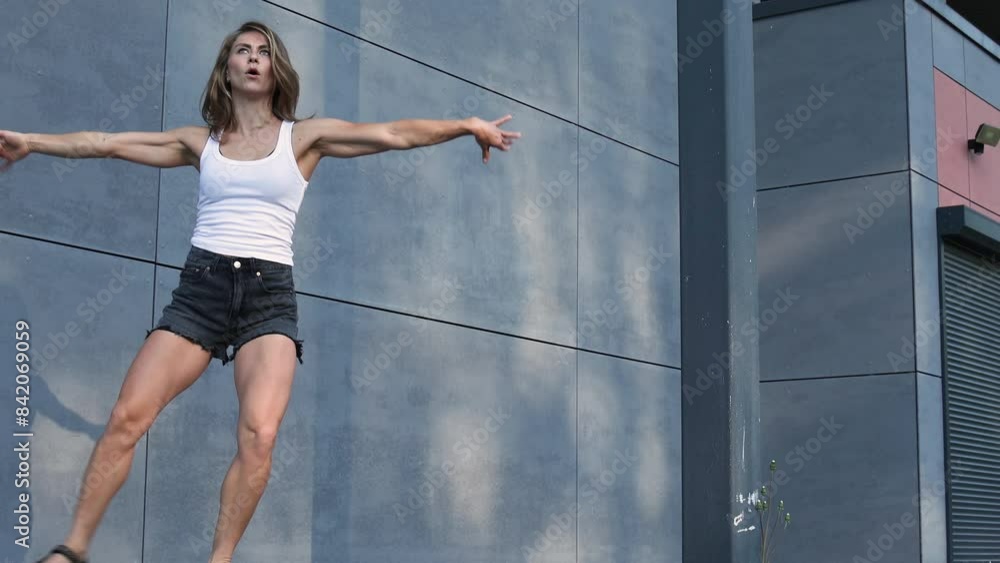 Actively dancing woman in shorts and a white T-shirt, athletic build, on a gray background, on the street. Stretching. International dance day Actively dancing woman in shorts and a white T-shirt, athletic build, on a gray background, on the street. Stretching. International dance day