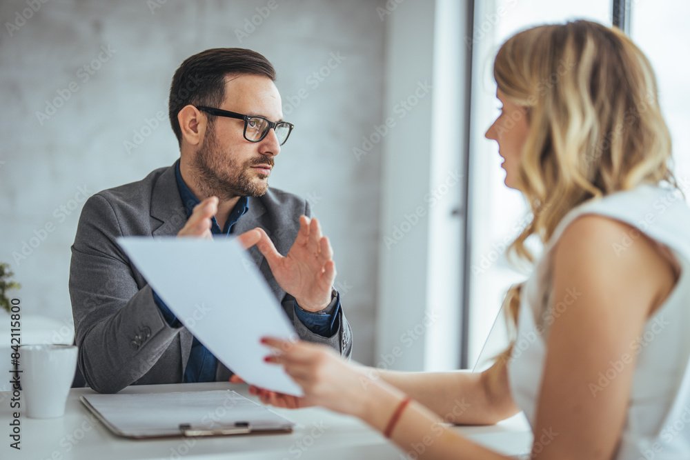 A confident Caucasian businesswoman discusses documents with a focused businessman in a well-lit office, exemplifying teamwork and collaboration. A confident Caucasian businesswoman discusses documents with a focused businessman in a well-lit office, exemplifying teamwork and collaboration.