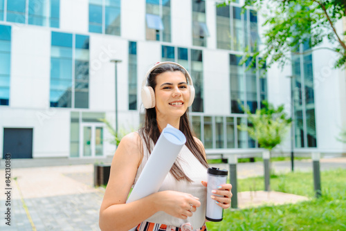 Free Download One young caucasian woman student going to university while listening to music on wireless headphones and holding papers and coffee	 - GFXLoad