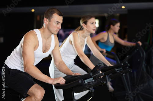 Sportive young man doing spin bike exercises in well-equipped gym during training session