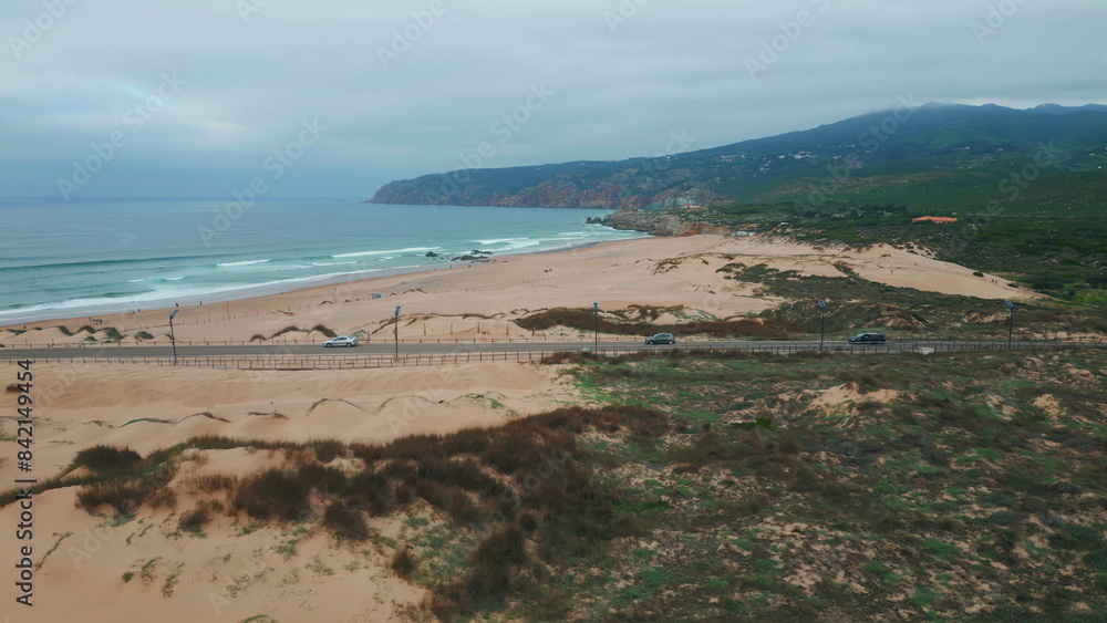 Foamy waves washing beach lined with sandy dunes drone view. Road stretching Foamy waves washing beach lined with sandy dunes drone view. Road stretching