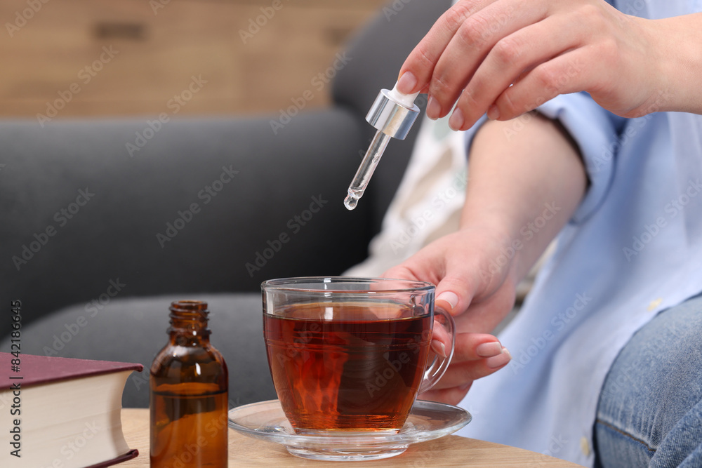 Woman dripping food supplement into cup of tea at wooden table indoors, closeup Woman dripping food supplement into cup of tea at wooden table indoors, closeup