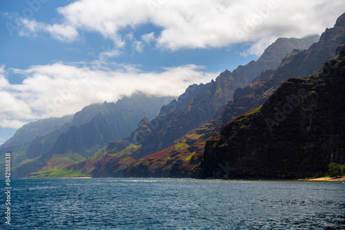 A breathtaking view of the rugged cliffs along the Na Pali Coast in Hawaii, showcasing vibrant green hills and dramatic rock formations above the turquoise ocean.