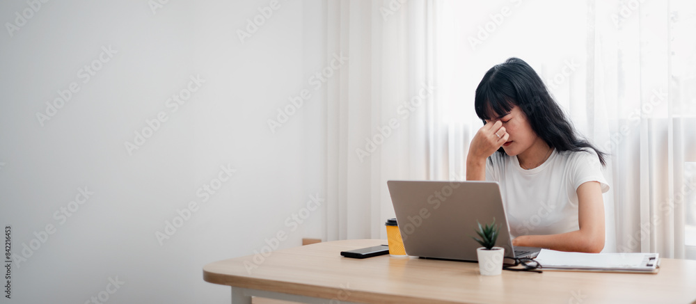 Young woman feeling stressed while working from home at a desk with a laptop and coffee in a modern minimalist home office setting. Young woman feeling stressed while working from home at a desk with a laptop and coffee in a modern minimalist home office setting.