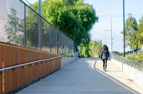 Background texture of an urban concrete pedestrian walkway with wooden panels and a metal railing, with a female walking on a paved path. © Doublelee