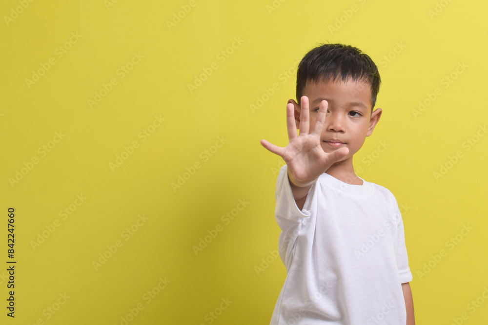 Image of Asian child posing raising his hand with five fingers, cute and smiling happily on a yellow background. portrait of an Asian boy. Copy space Image of Asian child posing raising his hand with five fingers, cute and smiling happily on a yellow background. portrait of an Asian boy. Copy space