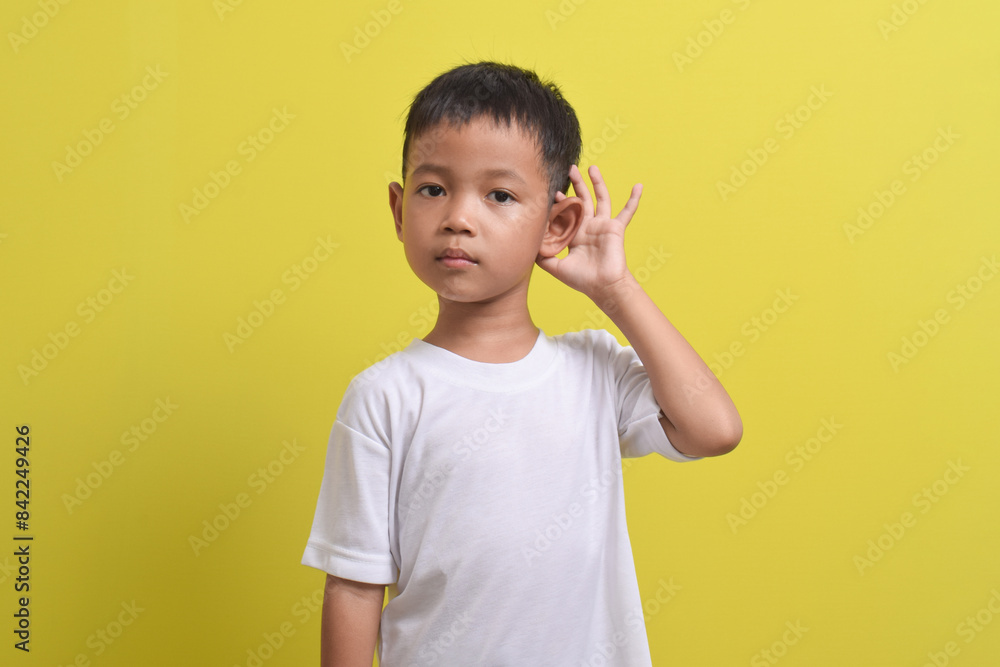 Image of Asian child trying to hear you listening attentively isolated on yellow background. portrait of an Asian boy posing cute and happy. Image of Asian child trying to hear you listening attentively isolated on yellow background. portrait of an Asian boy posing cute and happy.