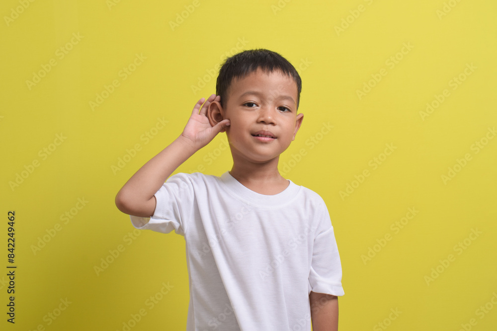 Image of Asian child trying to hear you listening attentively isolated on yellow background. portrait of an Asian boy posing cute and happy. Image of Asian child trying to hear you listening attentively isolated on yellow background. portrait of an Asian boy posing cute and happy.