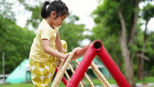 A young girl is playing on a playground with a rope ladder. She is smiling and she is enjoying herself