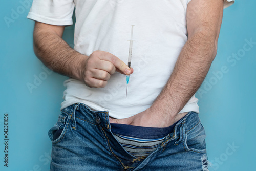 man holds a syringe in his hands and takes off his jeans. The concept of treatment of sexually transmitted diseases. Increased potency for porn actors.