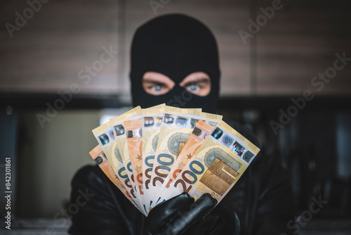 Arrested masked thief in balaclava with stolen money and raised arms isolated on white background. concept of crime, theft and illegal business, money laundering photo