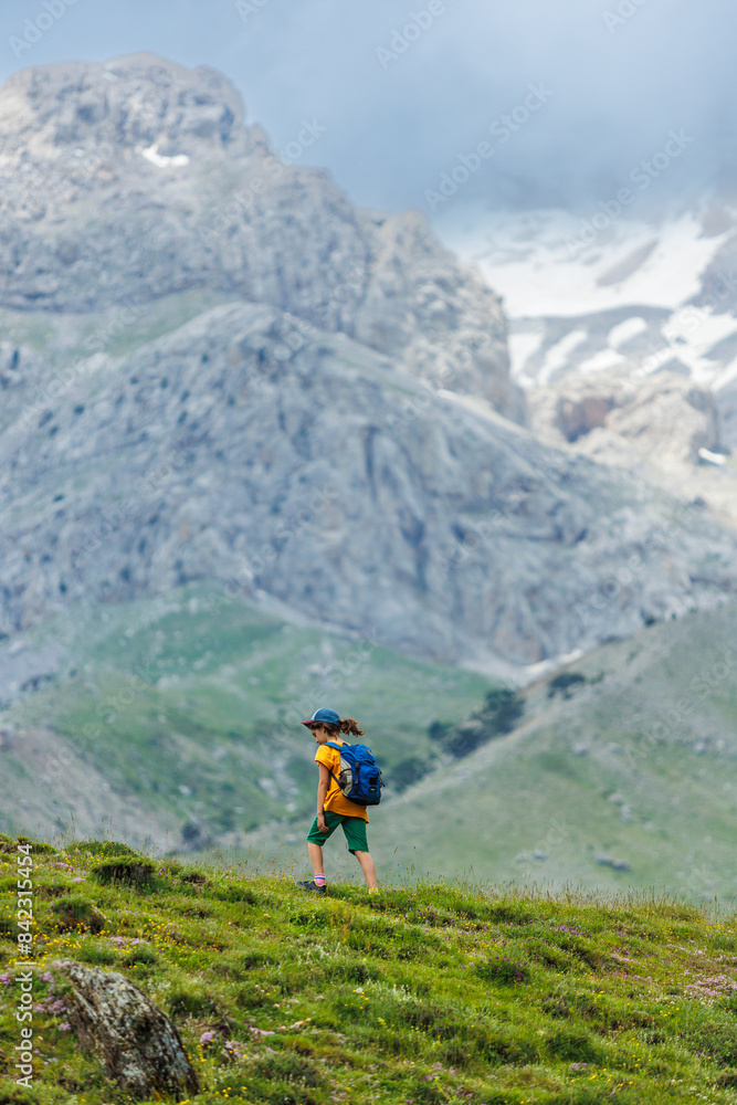 hiking in the mountains. A little boy with a backpack walks along a path against a background of mountains and clouds. Active healthy lifestyle on weekend hike journey. hiking in the mountains. A little boy with a backpack walks along a path against a background of mountains and clouds. Active healthy lifestyle on weekend hike journey.