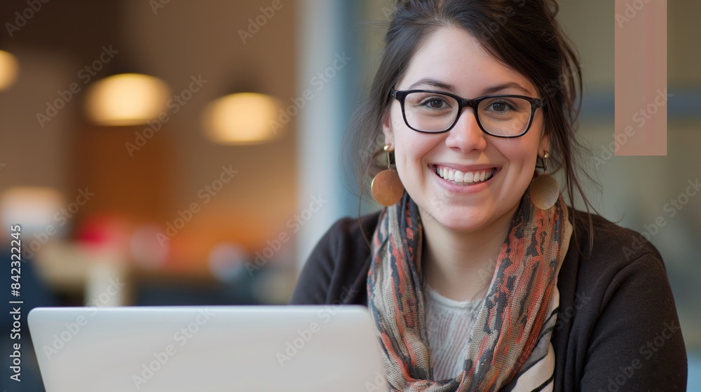 A young woman with glasses smiles while using her laptop at a cafe, exuding a casual professional vibe A young woman with glasses smiles while using her laptop at a cafe, exuding a casual professional vibe