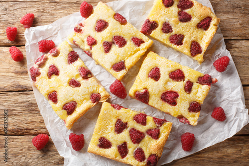 Delicious sweet dessert custard pie with fresh raspberries close-up on parchment on the table. Horizontal top view from above photo