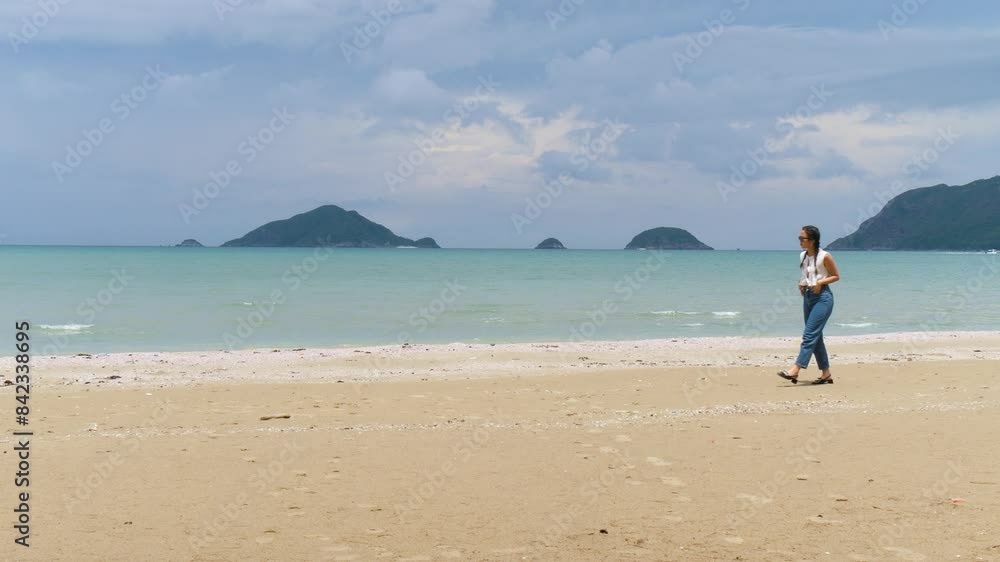 A woman walks along the serene beach of Con Dao island, Vietnam on a cloudy day A woman walks along the serene beach of Con Dao island, Vietnam on a cloudy day
