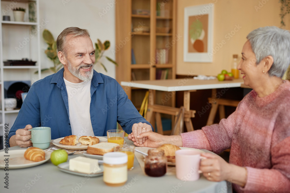 Portrait of happy senior couple holding hands at dinner table and enjoying breakfast together at home Portrait of happy senior couple holding hands at dinner table and enjoying breakfast together at home