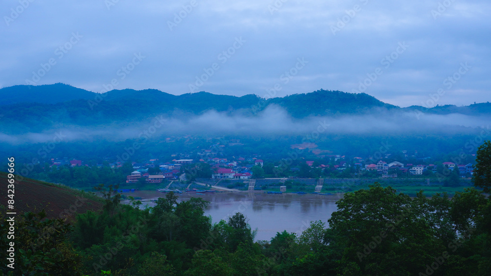 Aerial view of the mighty Mekong River winding from Chiang Khong, showing the vastness and beauty of the muddy waterway contrasting with the surrounding lush mountains and Laos villages.