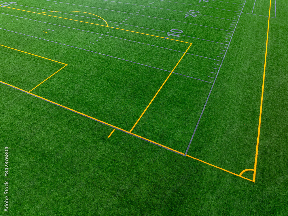 Obraz premium Late afternoon aerial photo of gray football line with yellow soccer lines on a artificial, synthetic turf field. 