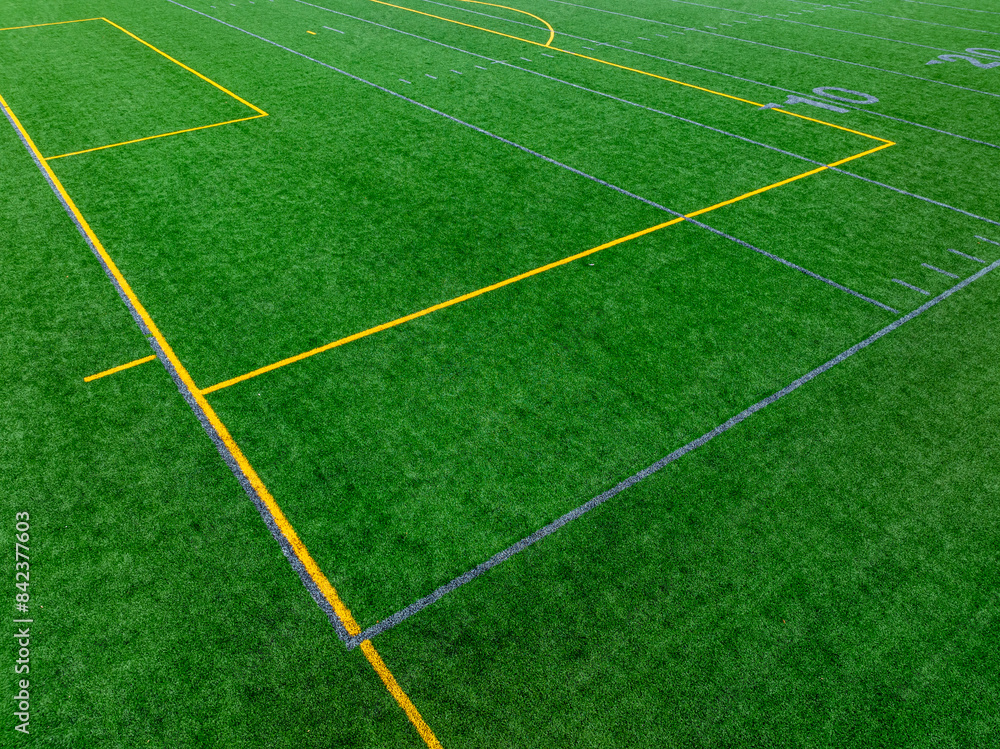 Obraz premium Late afternoon aerial photo of gray football line with yellow soccer lines on a artificial, synthetic turf field. 