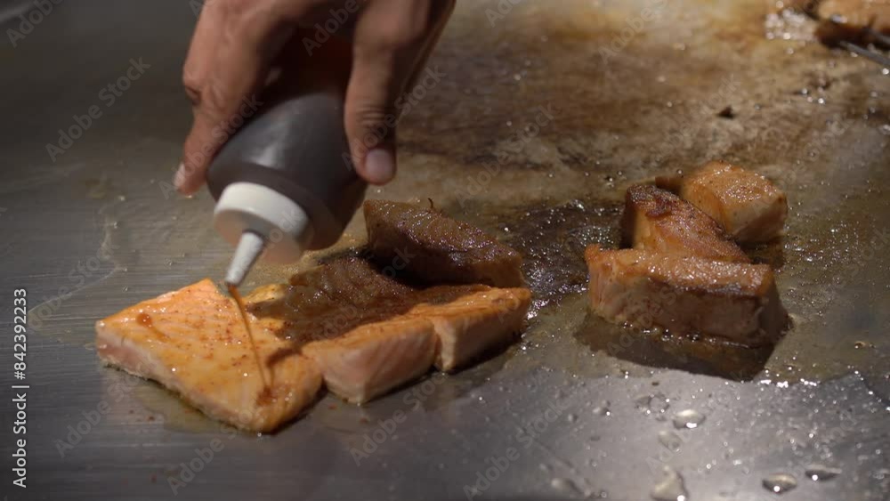Chef's hand preparing salmon steak on teppanyaki grill Chef's hand preparing salmon steak on teppanyaki grill
