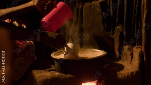 Young african woman prepares food on fireplace in twig hut. Traditional dishes are prepared for whole family in large quantities