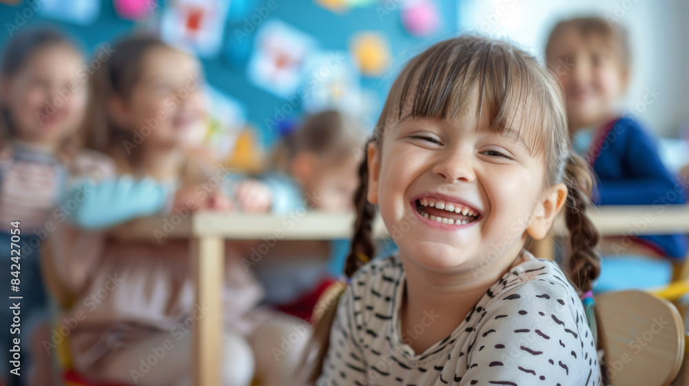 A schoolgirl, a disabled girl with developmental disabilities, smiles while sitting at a desk in a school classroom against the backdrop of other students. Inclusivity. A schoolgirl, a disabled girl with developmental disabilities, smiles while sitting at a desk in a school classroom against the backdrop of other students. Inclusivity.
